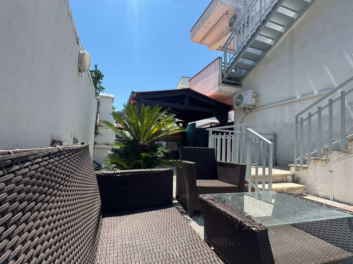 Spazio esterno di una villa in vendita a Milazzo con mobili da esterno e piante tropicali sotto un cielo sereno.