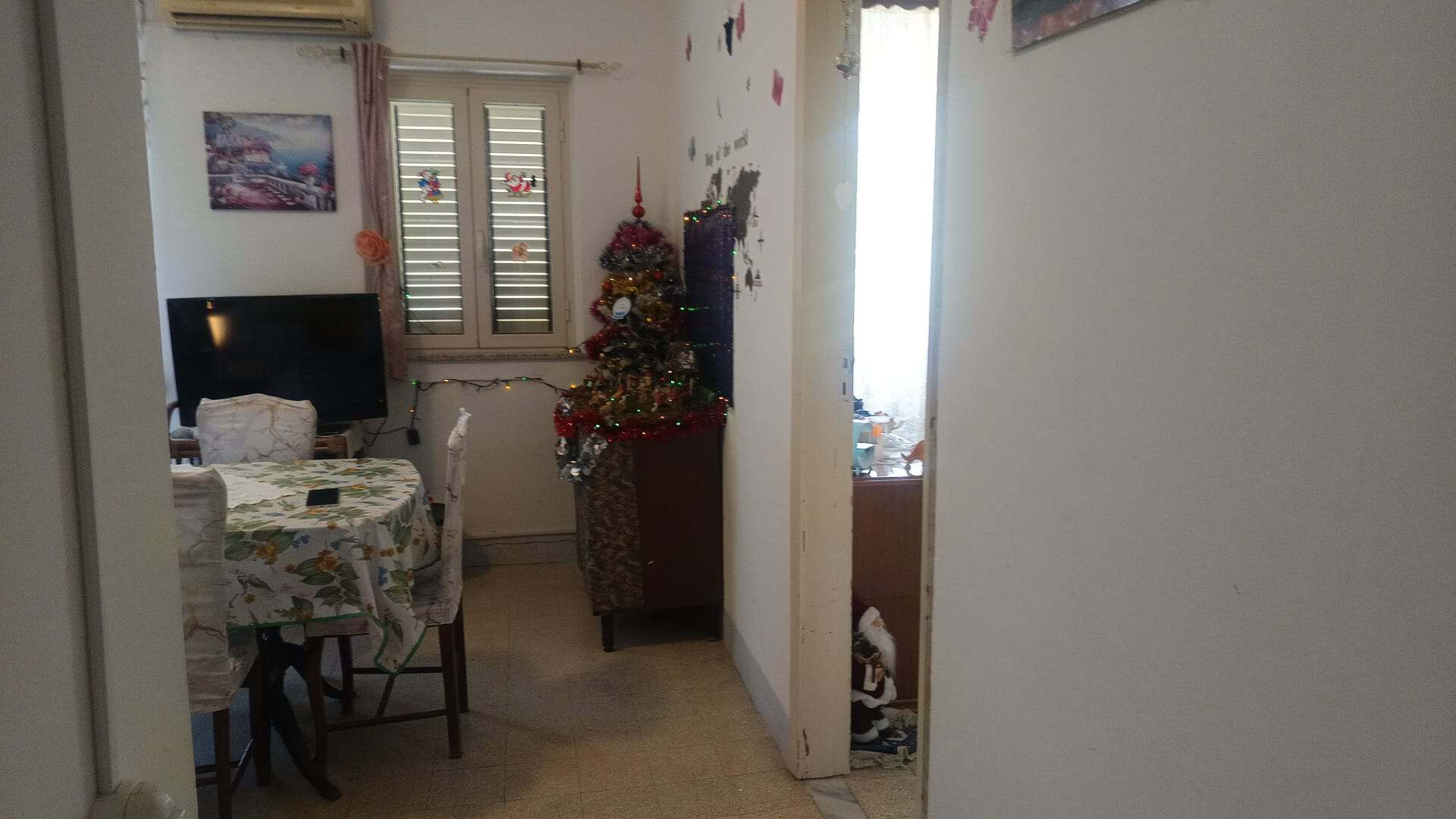 Interno di un appartamento con soggiorno e zona pranzo, decorato per le festività natalizie, con un albero di Natale e mobili in stile semplice.