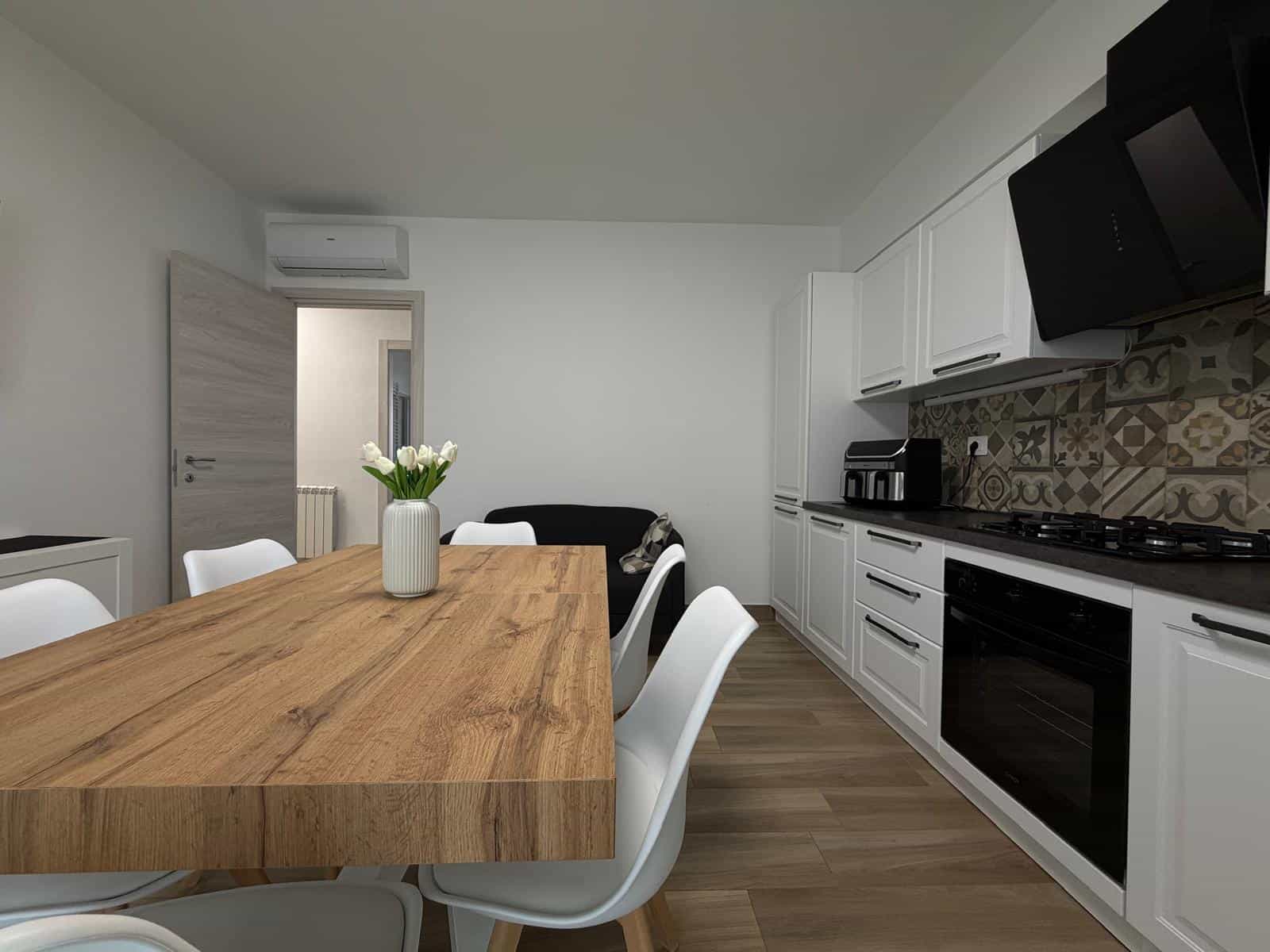 Cucina moderna con mobili bianchi, piano in legno e pareti decorate con piastrelle colorate, ambiente luminoso e accogliente.