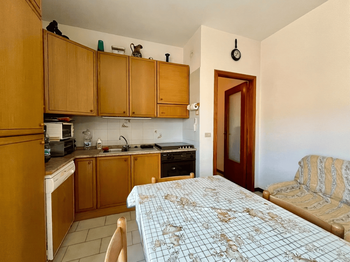 Cucina compatta con mobili in legno, tavolo da pranzo e divano in soggiorno, in un appartamento in vendita a Oliveri, Me.