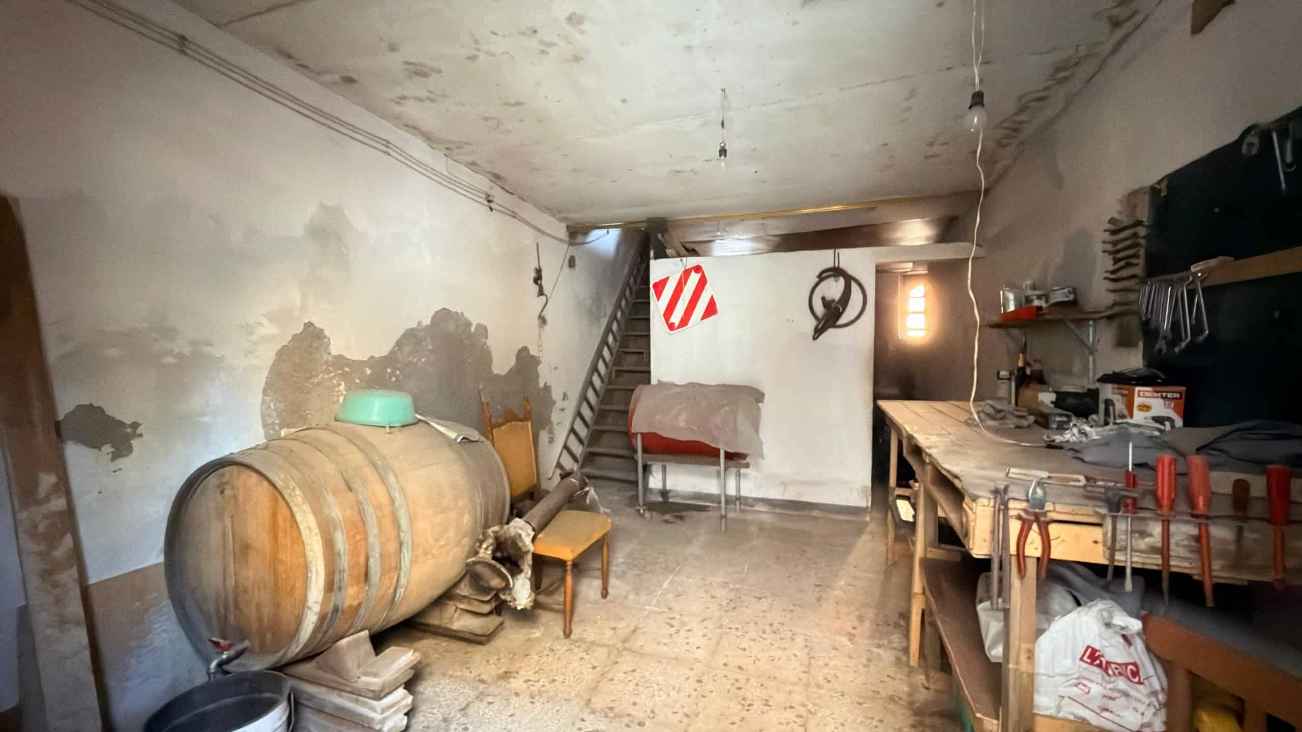 Interno di un garage o magazzino in condizioni di abbandono con pareti danneggiate e attrezzature sparse.