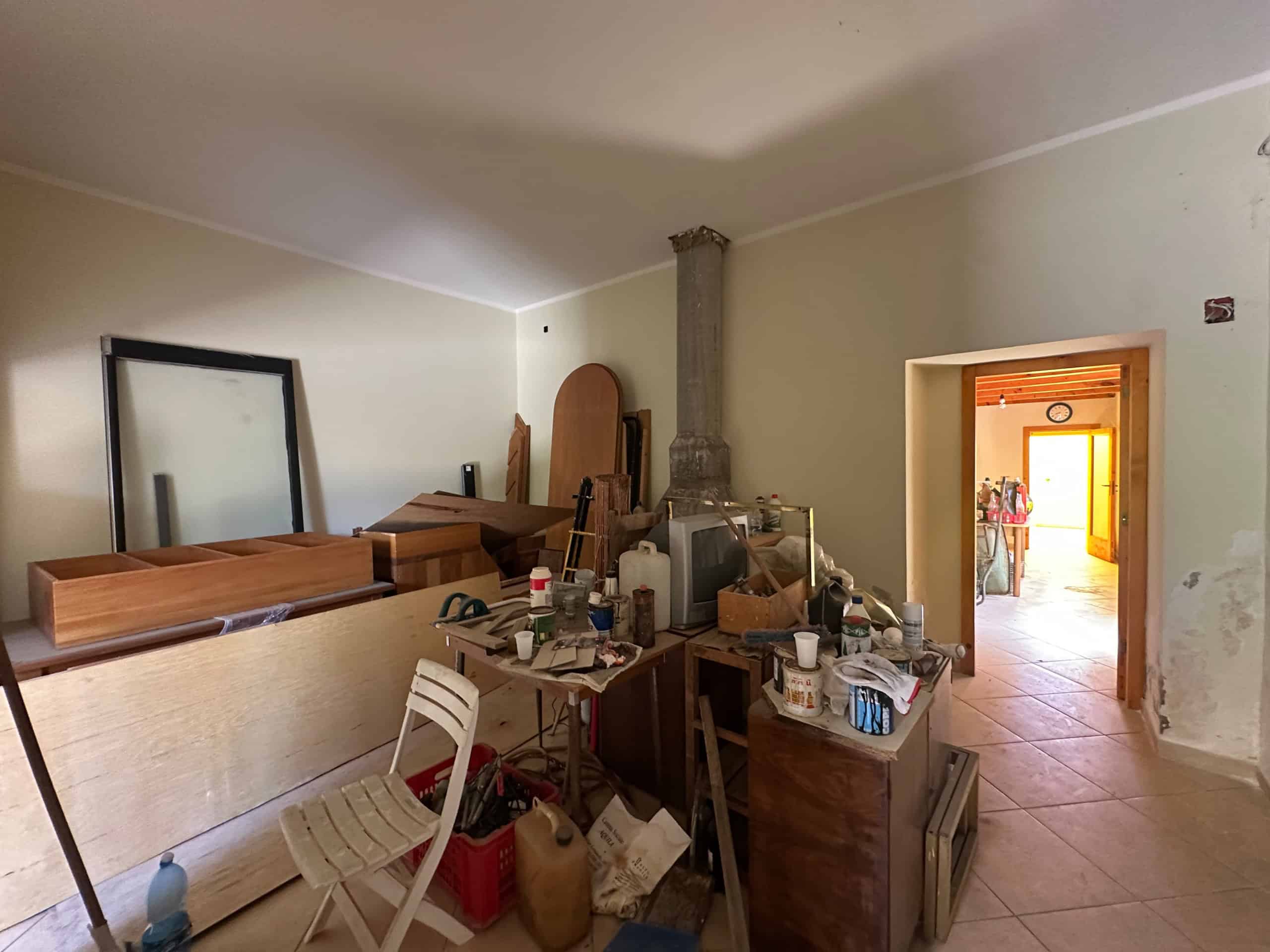 Interno di una casa in vendita a Milazzo con mobili e oggetti disordinati, pareti chiare e porta che conduce a un'altra stanza.