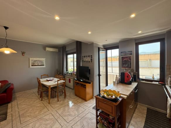Interno di un appartamento con soggiorno e cucina, con grandi finestre e arredamento moderno.