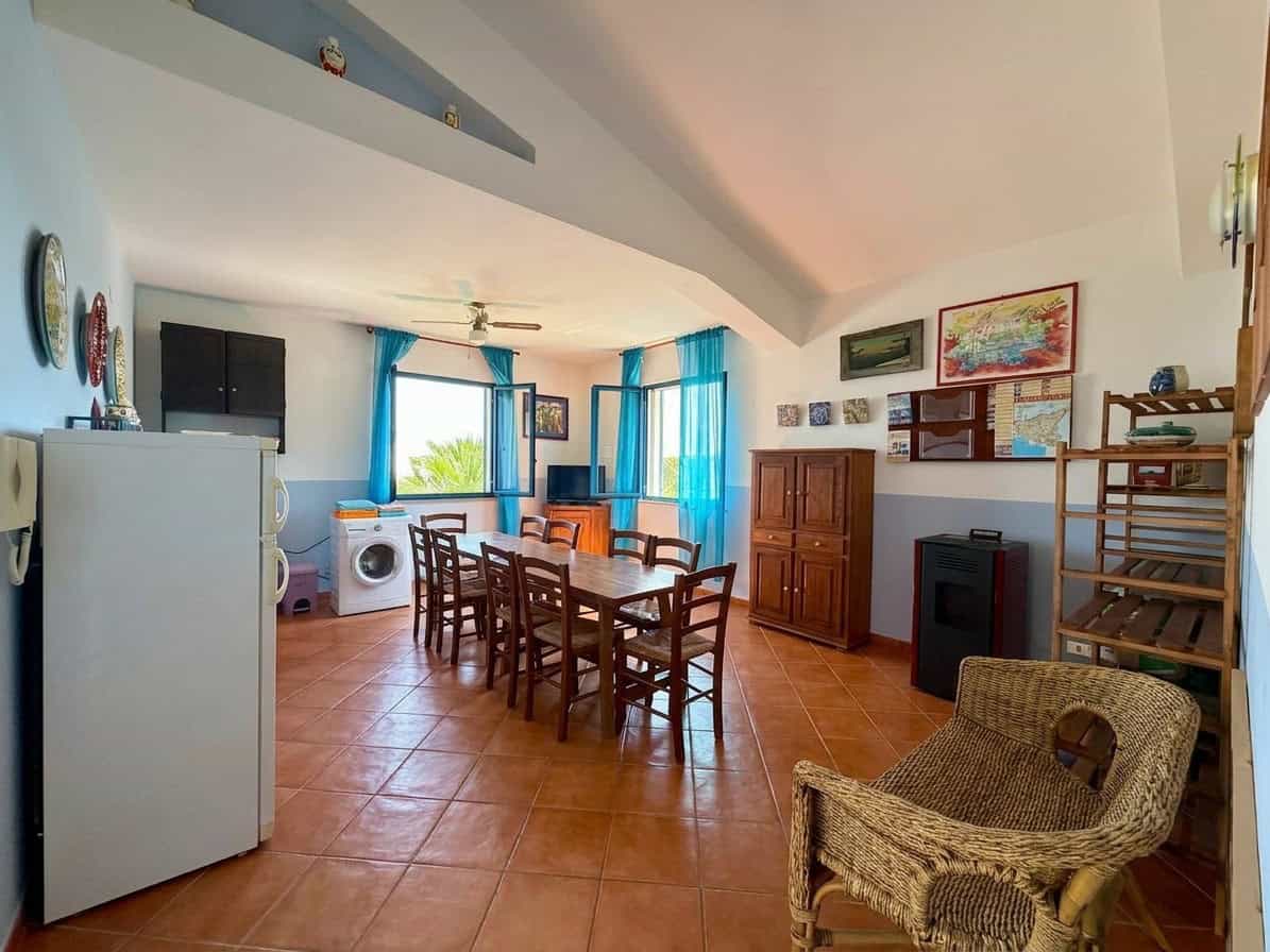 Interno di una casa con zona pranzo, mobili in legno, pareti decorate e grandi finestre con tende azzurre, ambiente luminoso e accogliente.