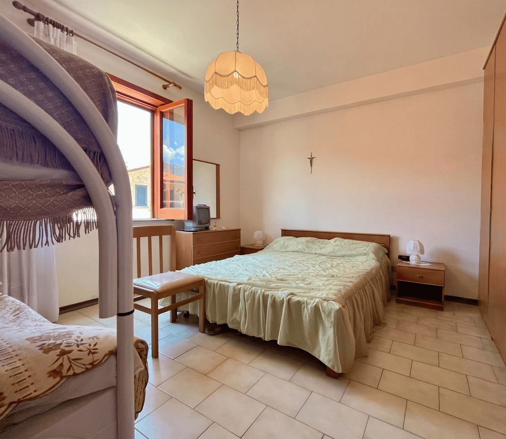 Camera che mostra una camera da letto luminosa con letto matrimoniale, armadio, finestra aperta e decorazioni semplici.