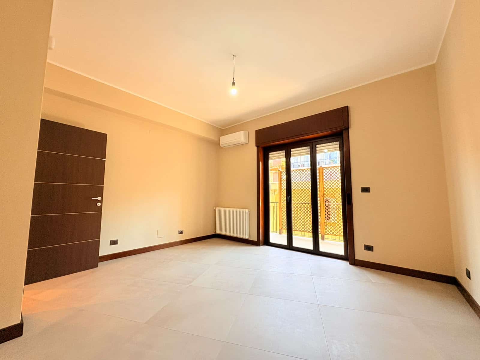 Ampio soggiorno luminoso con porta finestra che dà su un balcone, pareti beige e pavimento chiaro.