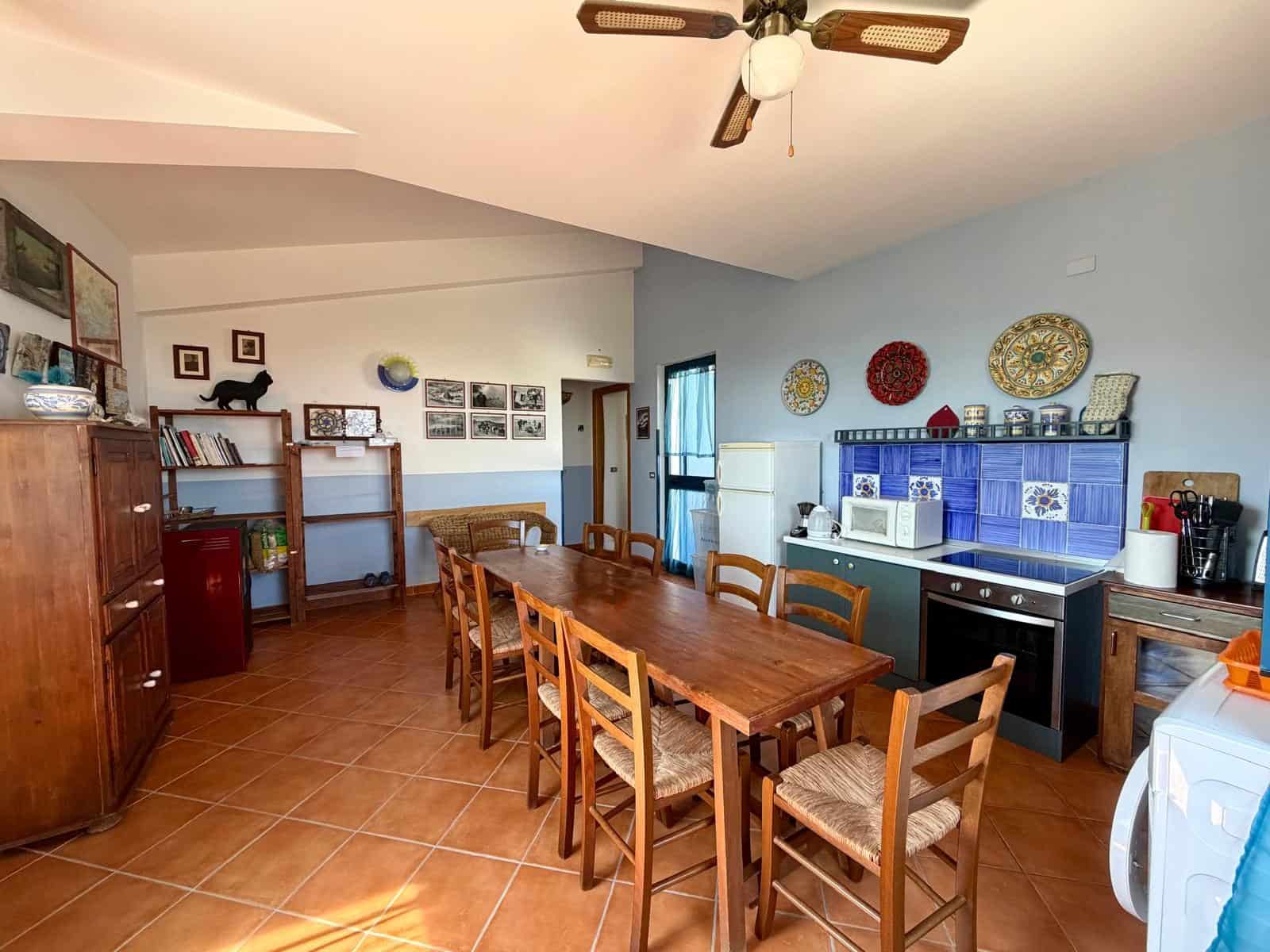 Interno di una cucina spaziosa con tavolo in legno e sedie, pareti decorate con piastrelle colorate e oggetti d'arredo, ambiente luminoso e accogliente.