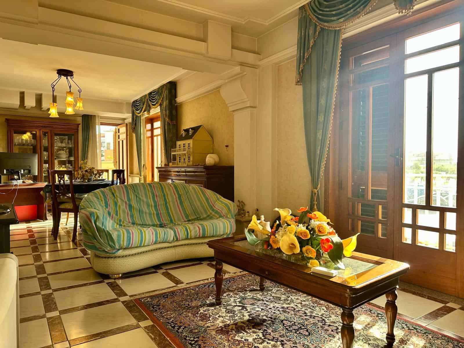 Interno di un soggiorno elegante con divano, tavolo con fiori e grandi finestre con tende blu.