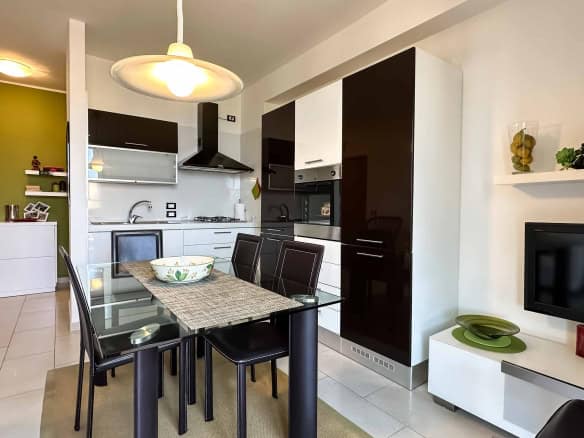Interno di un appartamento moderno con cucina a vista, zona pranzo e soggiorno, arredamento elegante e colori neutri.