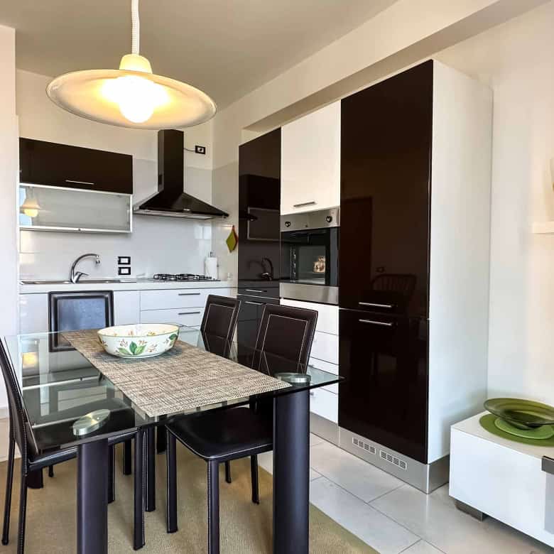 Interno di un appartamento moderno con cucina a vista, zona pranzo e soggiorno, arredamento elegante e colori neutri.