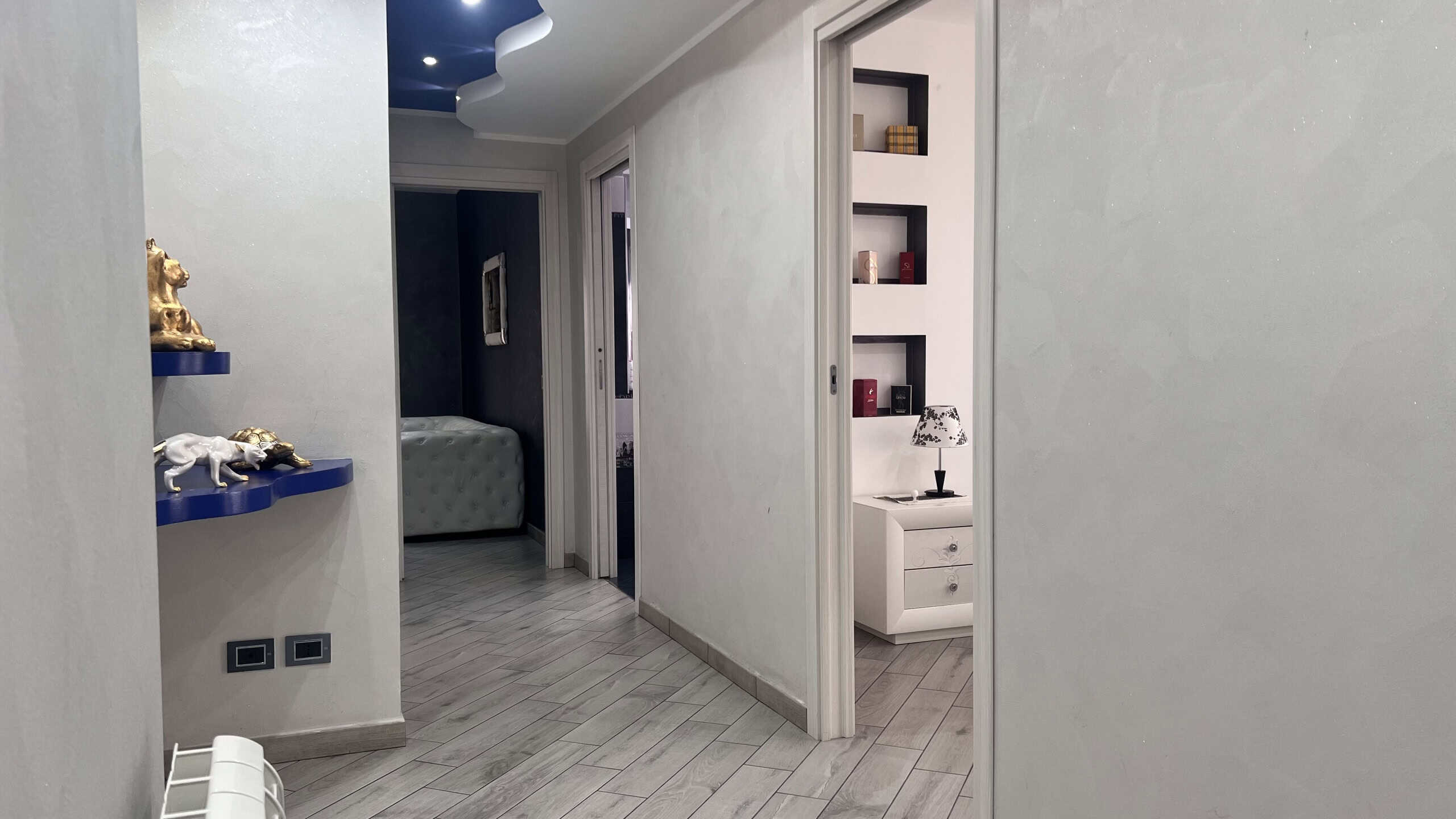 Interno di un appartamento in vendita a Messina, con pareti bianche, pavimento in piastrelle e arredi eleganti, inclusa una libreria e un angolo con decorazioni.