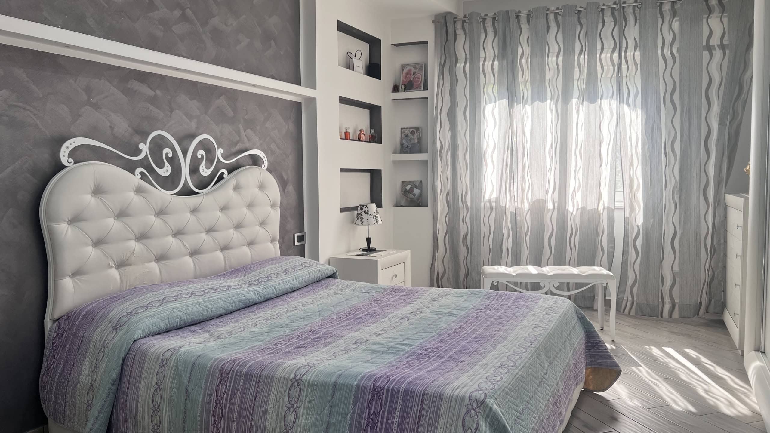 Camera da letto moderna con letto imbottito e tende leggere, ambiente luminoso e accogliente.