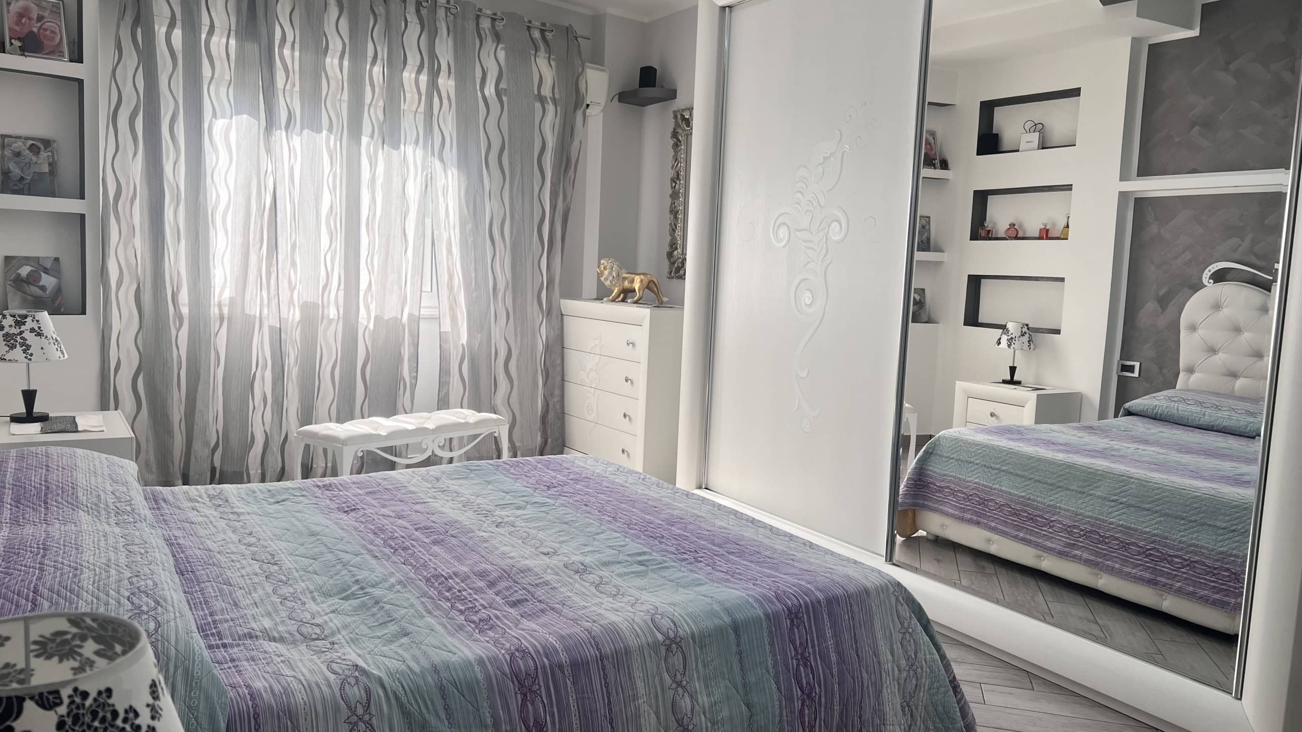 Interno di una camera da letto moderna con letto matrimoniale, armadio a specchio e decorazioni eleganti, in un appartamento in vendita in Via Adolfo Celi 50, Messina.