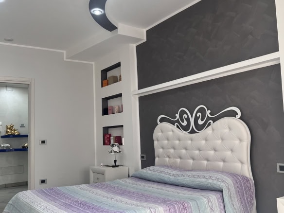 Camera che mostra una camera da letto moderna con pareti bianche e una testiera imbottita bianca, decorazioni nere e nicchie con oggetti decorativi.