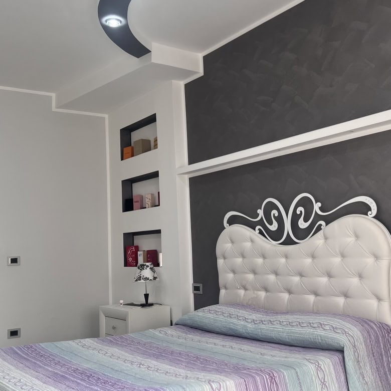 Camera che mostra una camera da letto moderna con pareti bianche e una testiera imbottita bianca, decorazioni nere e nicchie con oggetti decorativi.