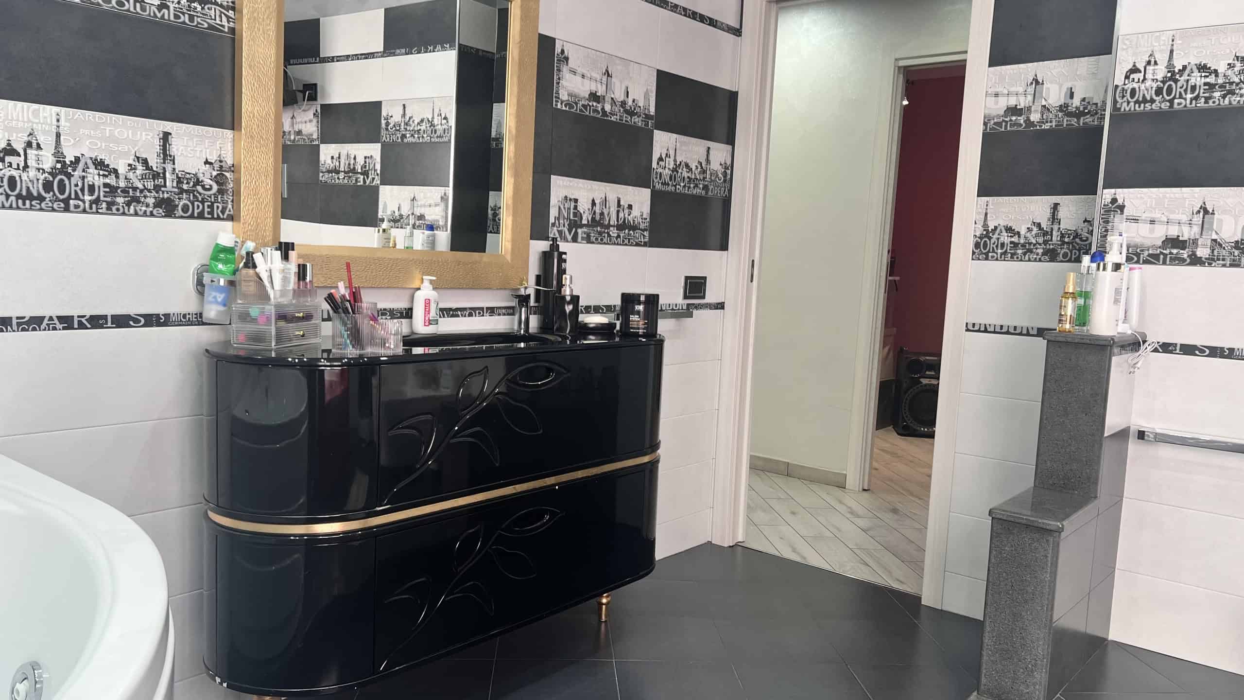 Interno di un bagno moderno con lavabo nero, specchio grande e pareti decorate con foto di città in bianco e nero.