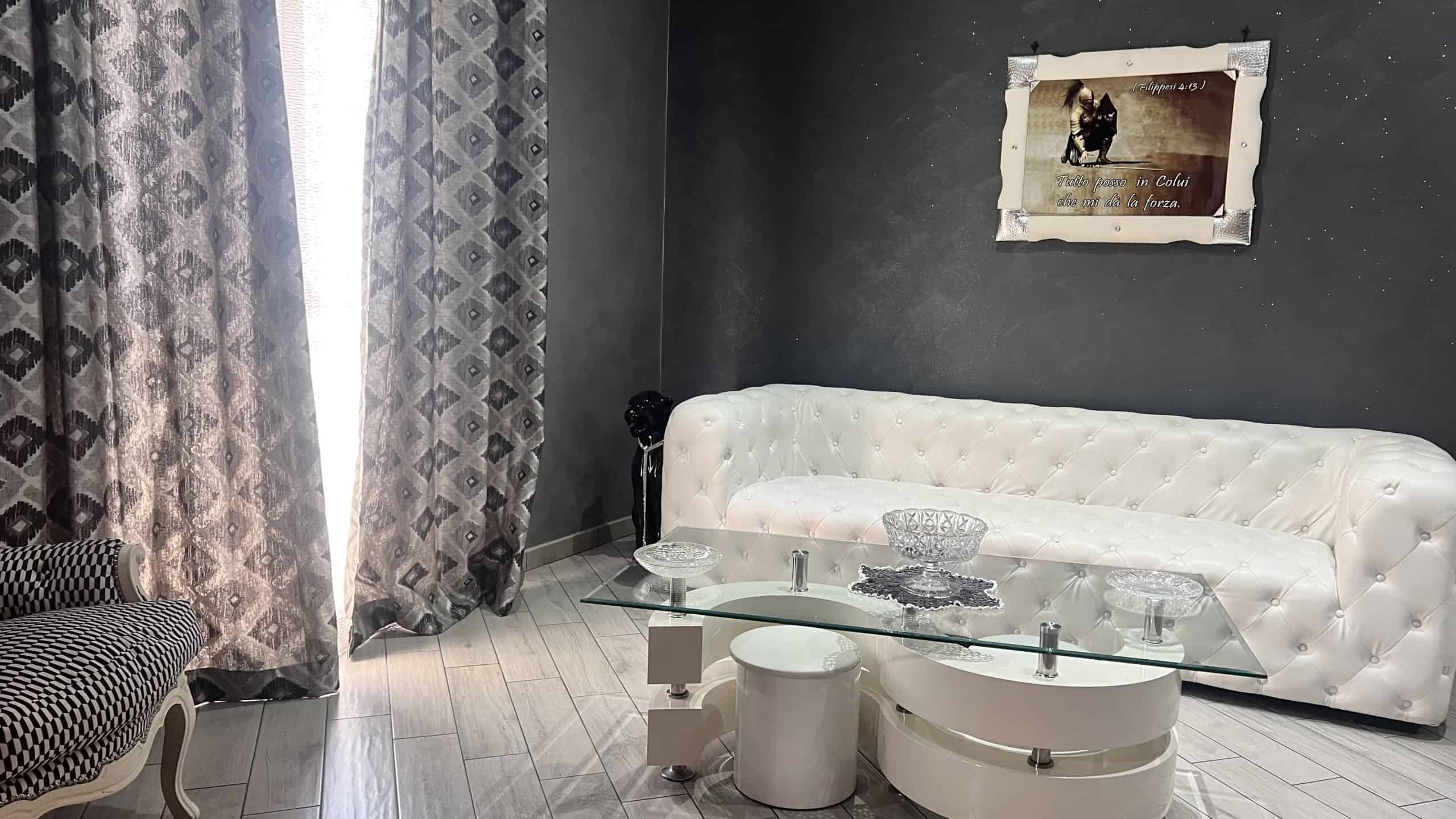 Interno di un salotto moderno con divano bianco, tavolino in vetro e tende decorative, in un appartamento in vendita a Messina.