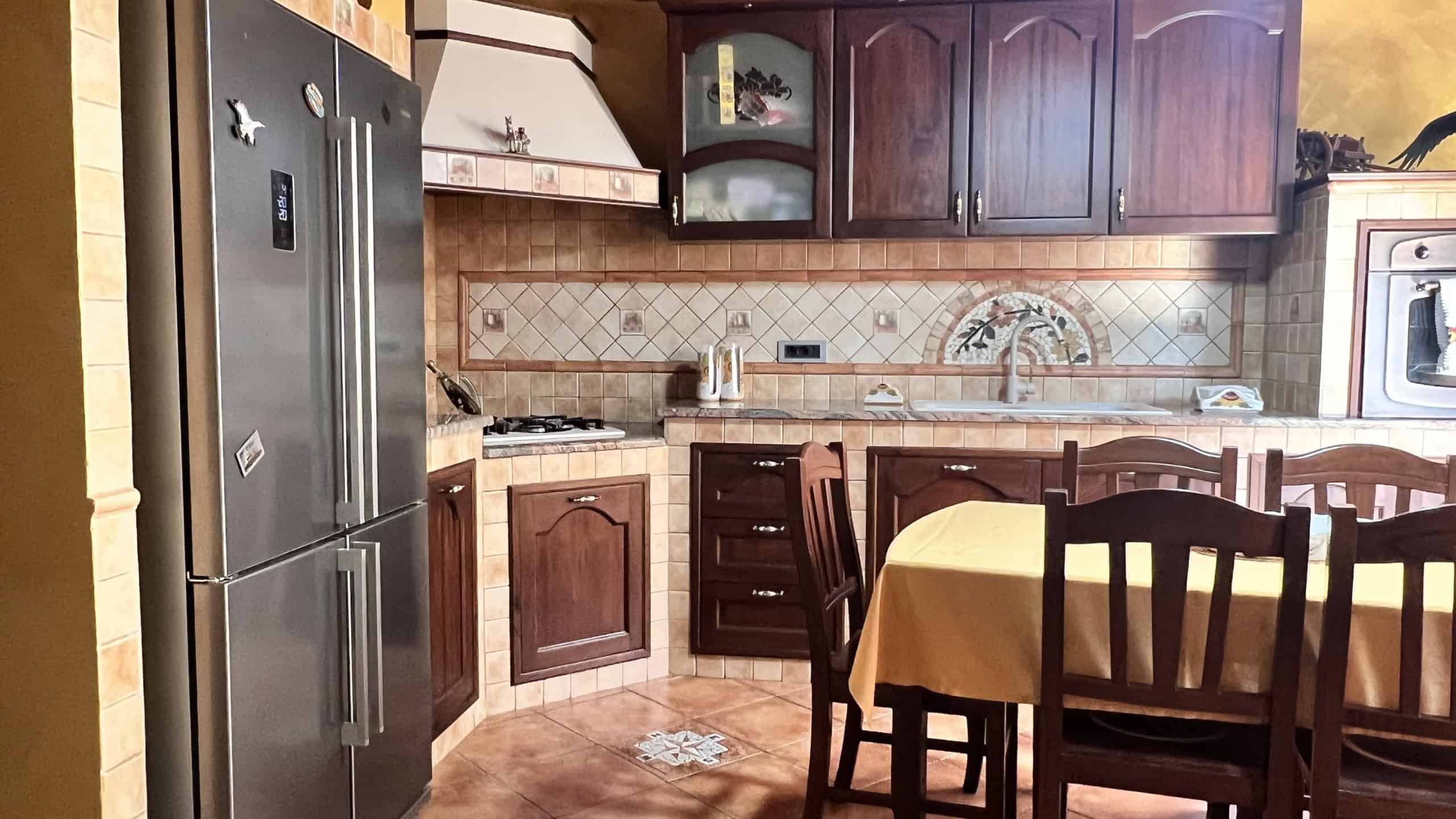 Cucina abitabile con mobili in legno scuro, piano cottura e zona pranzo in un appartamento in vendita a Messina.