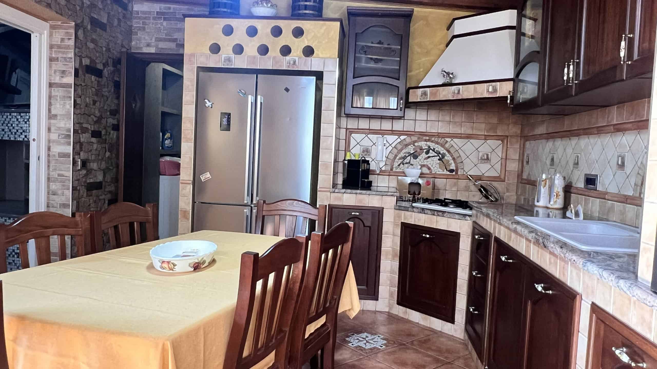 Interno di una cucina moderna con mobili in legno scuro, frigorifero in acciaio inox e piano cottura a gas, in un appartamento in vendita a Messina.