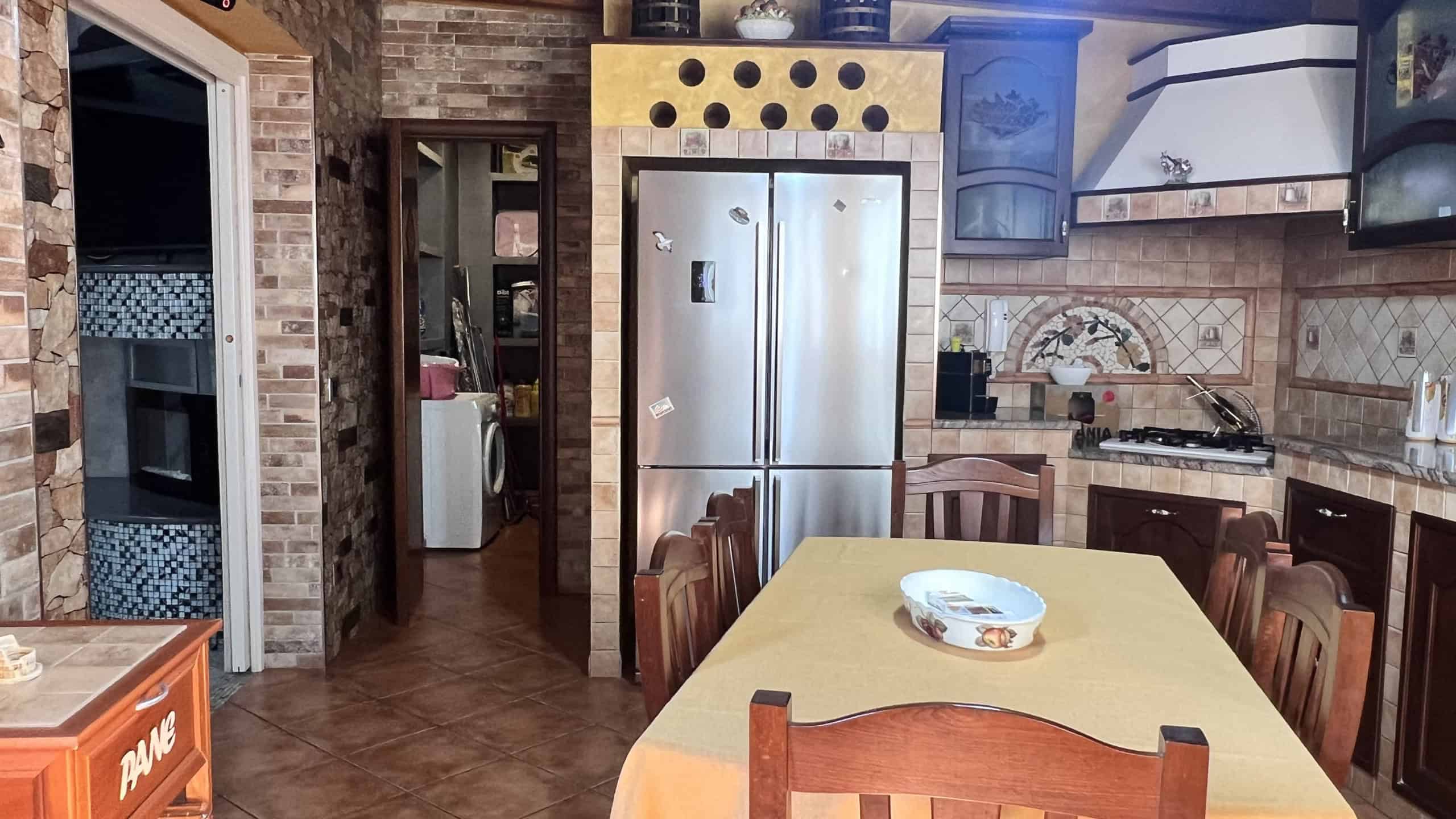 Interno di una cucina moderna con mobili in legno, frigorifero in acciaio inox e dettagli decorativi in ceramica, in un appartamento in vendita a Messina.