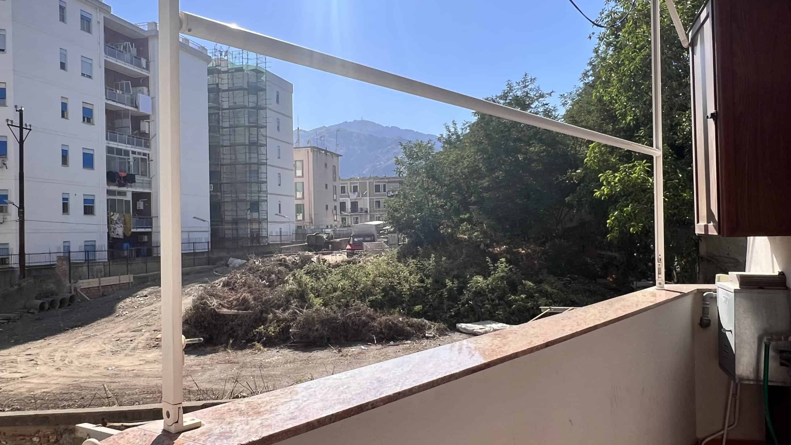 Balcone di un appartamento con vista su edifici moderni e montagne sullo sfondo, in zona urbana di Messina.