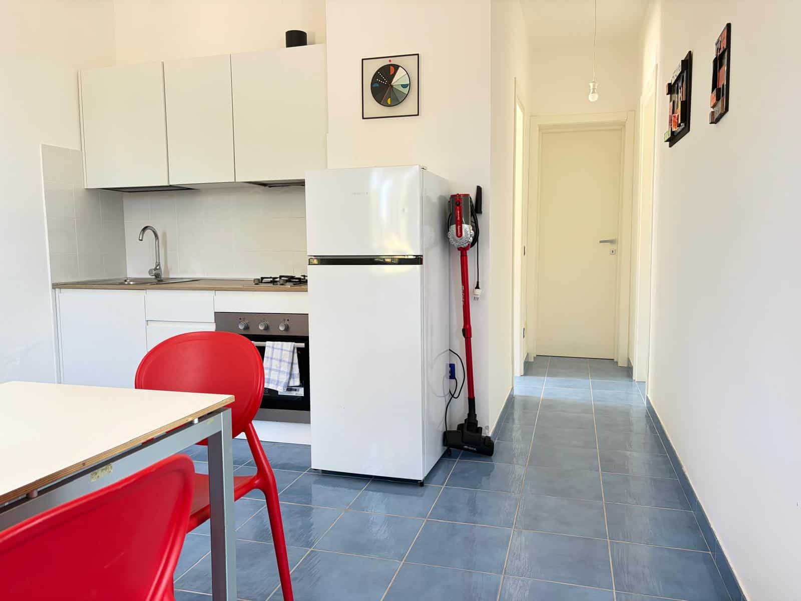 Cucina moderna con frigorifero, forno e mobili bianchi, in un ambiente luminoso e pulito.