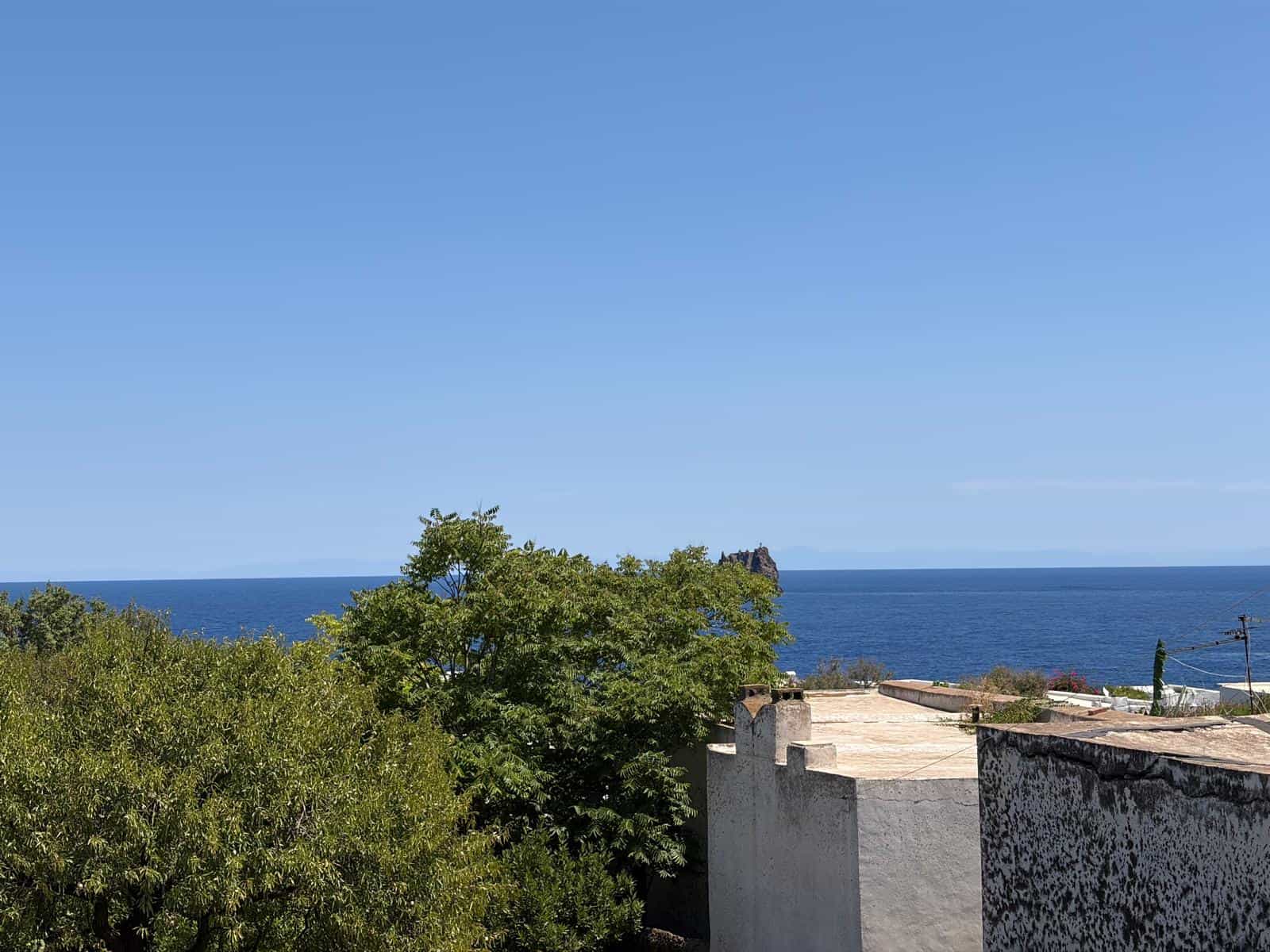 Paesaggio costiero con mare, cielo azzurro e vegetazione verde, vista da un'area residenziale vicino alla costa.