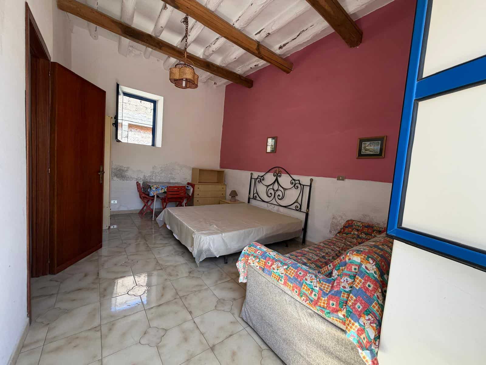 Camera angolare di una stanza da letto con pareti rosa e bianca, letto matrimoniale, divano colorato e soffitto con travi in legno.