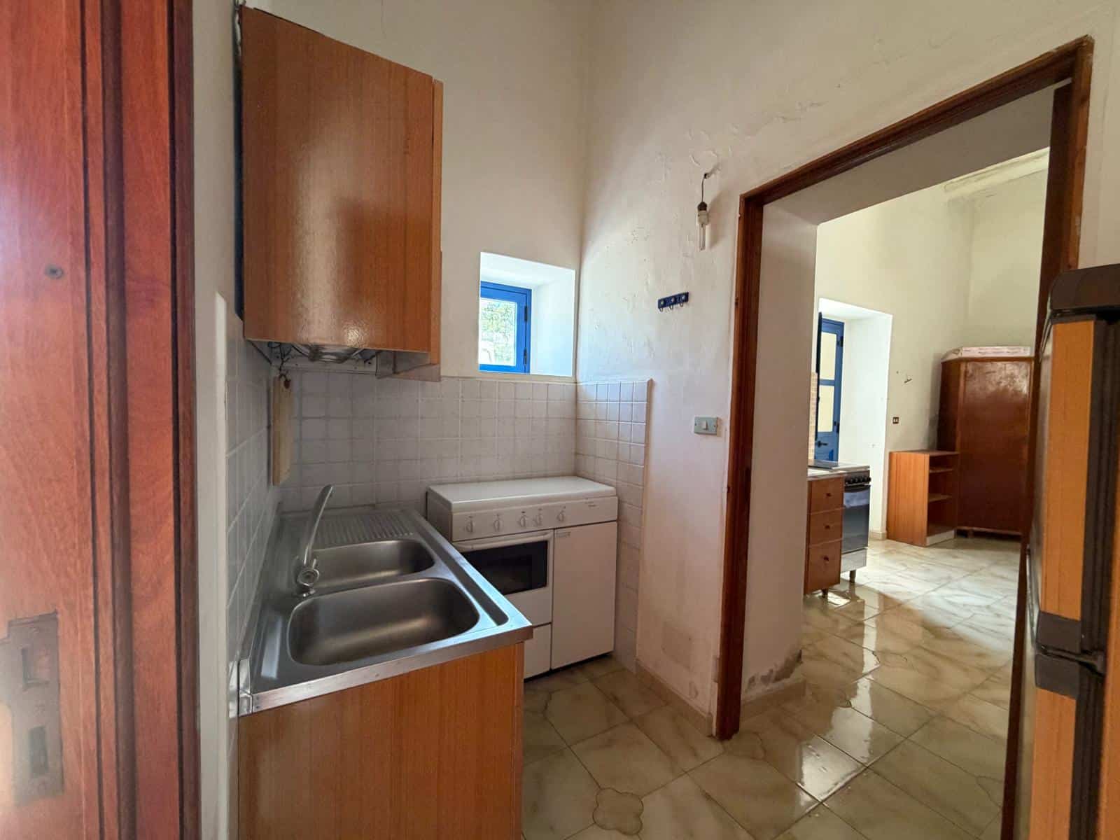 Cucina compatta con lavabo, forno e armadietti in legno, finestra e porta che conduce a un'altra stanza.