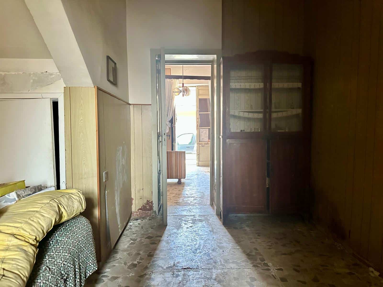 Interno di una casa indipendente con pareti in legno e pavimento in pietra, vista verso l'ingresso e una stanza luminosa.