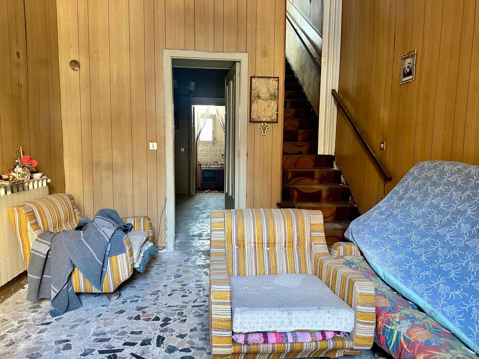 Interno di una casa indipendente con mobili vintage, pareti in legno e scala in legno che porta al piano superiore.
