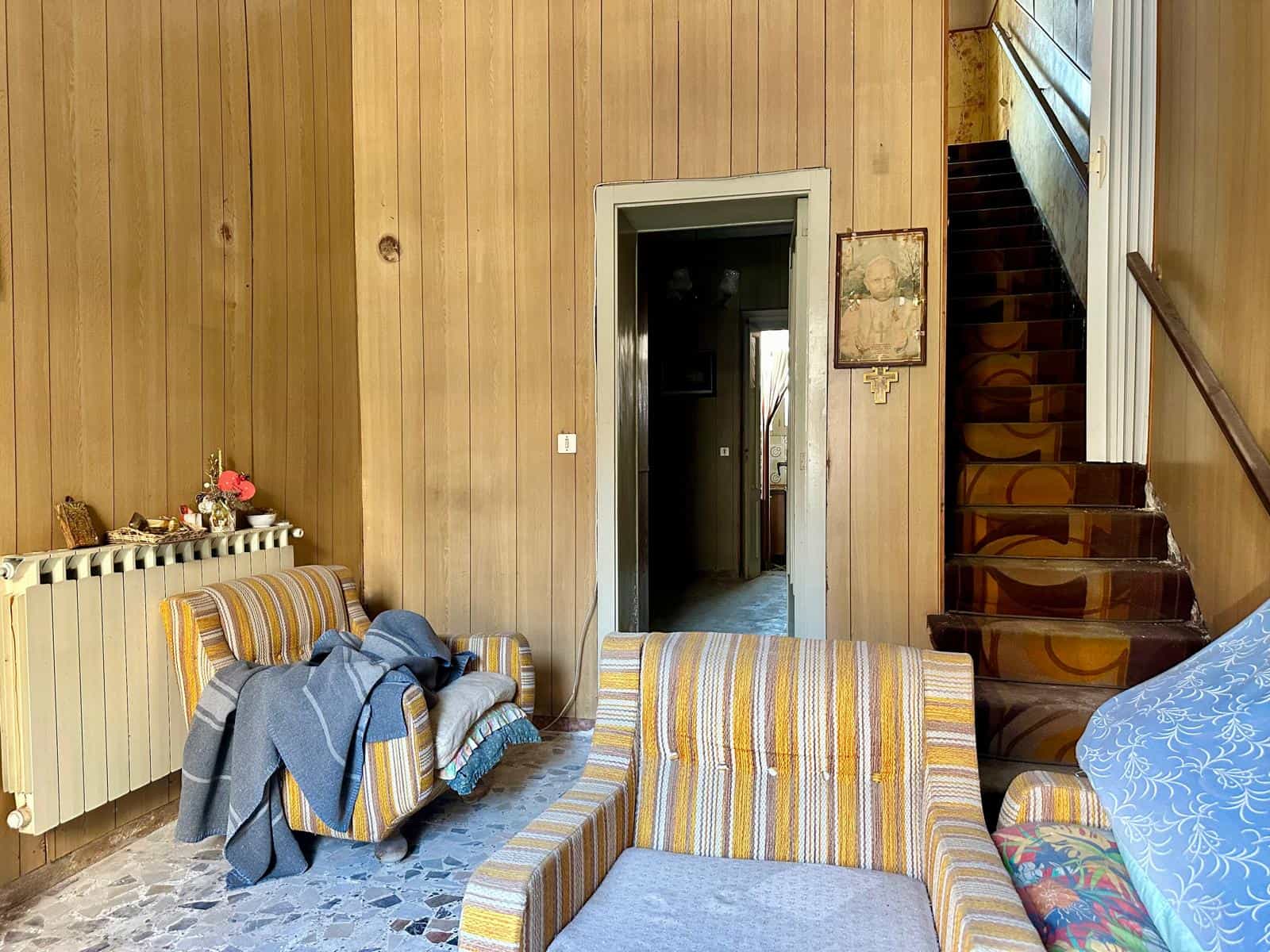 Interno di una casa indipendente con divani e scala in legno, stile vintage, pareti in legno chiaro.