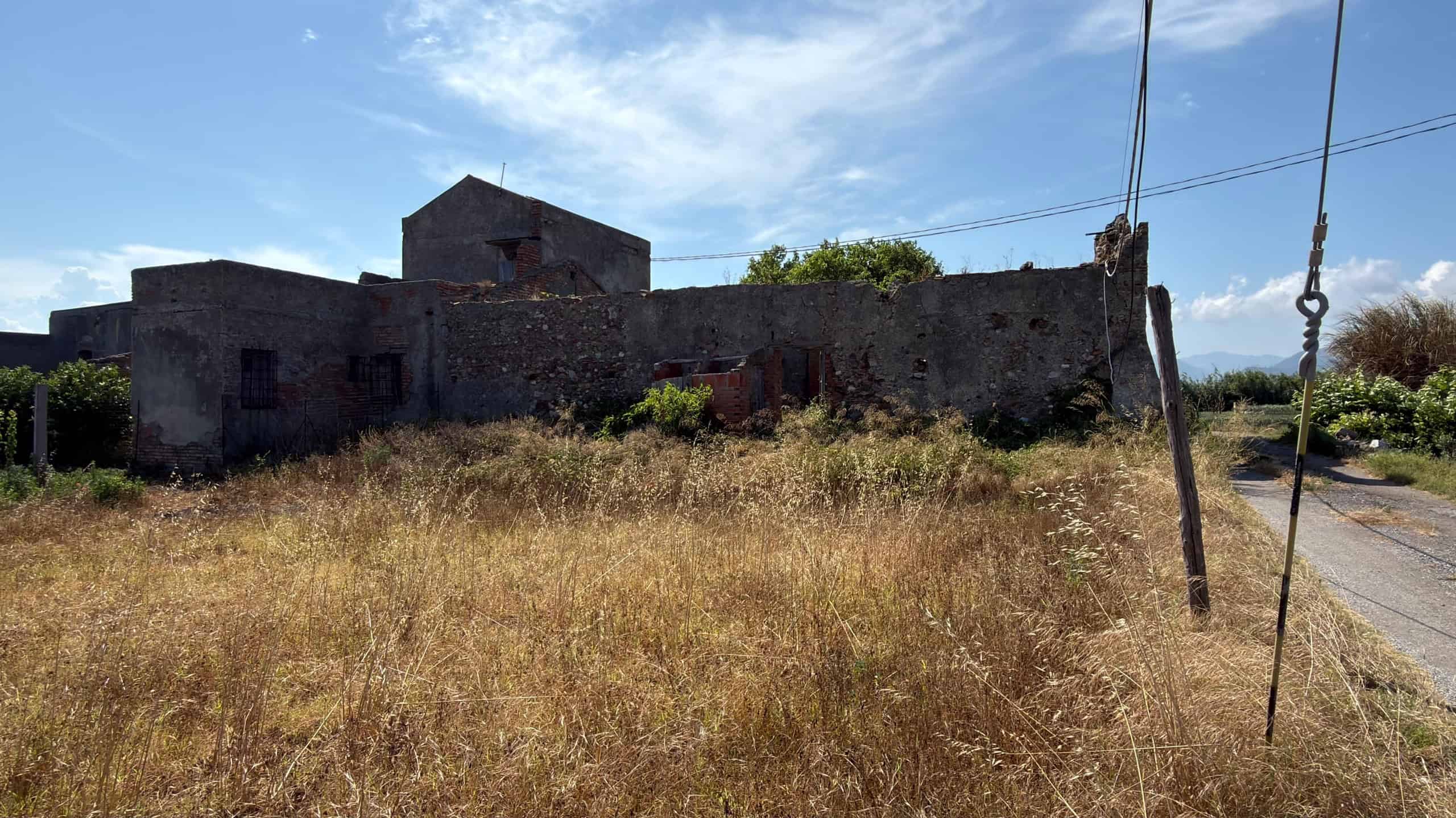 Edificio abbandonato in campagna con muri di pietra e vegetazione secca, scenario rurale in Italia.