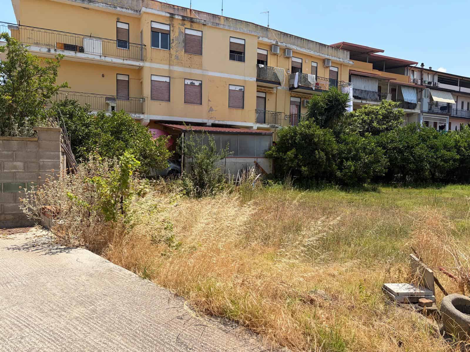 Terreno edificabile in vendita a Oliveri, con vista su edificio residenziale e vegetazione circostante.