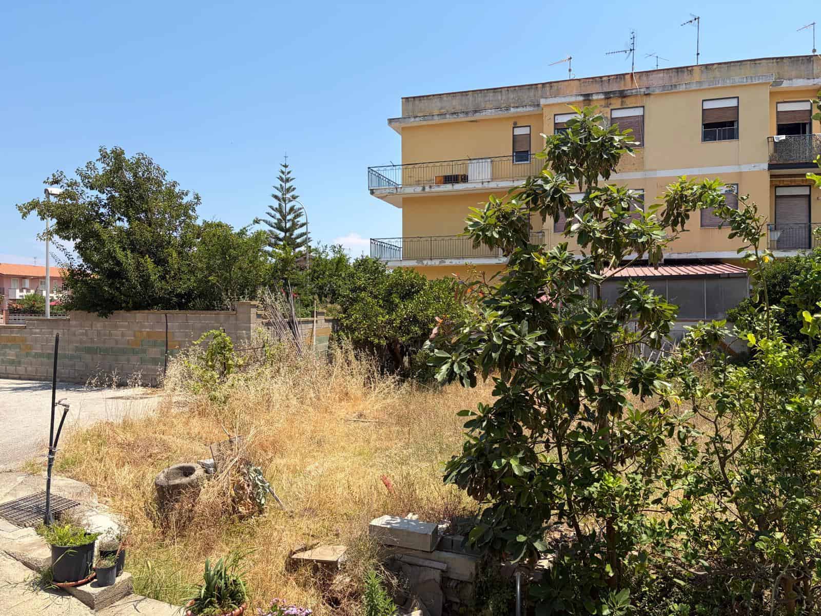 Terreno edificabile in vendita a Oliveri, con vegetazione e vicino a edificio residenziale, ideale per costruzioni.