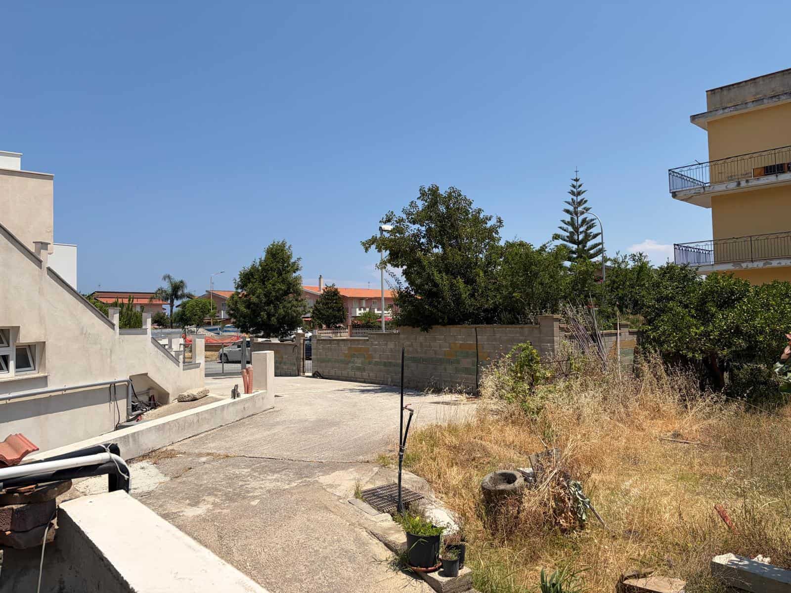 Terreno edificabile in vendita a Oliveri, con spazio aperto e vegetazione, vicino a edifici residenziali e strada principale.