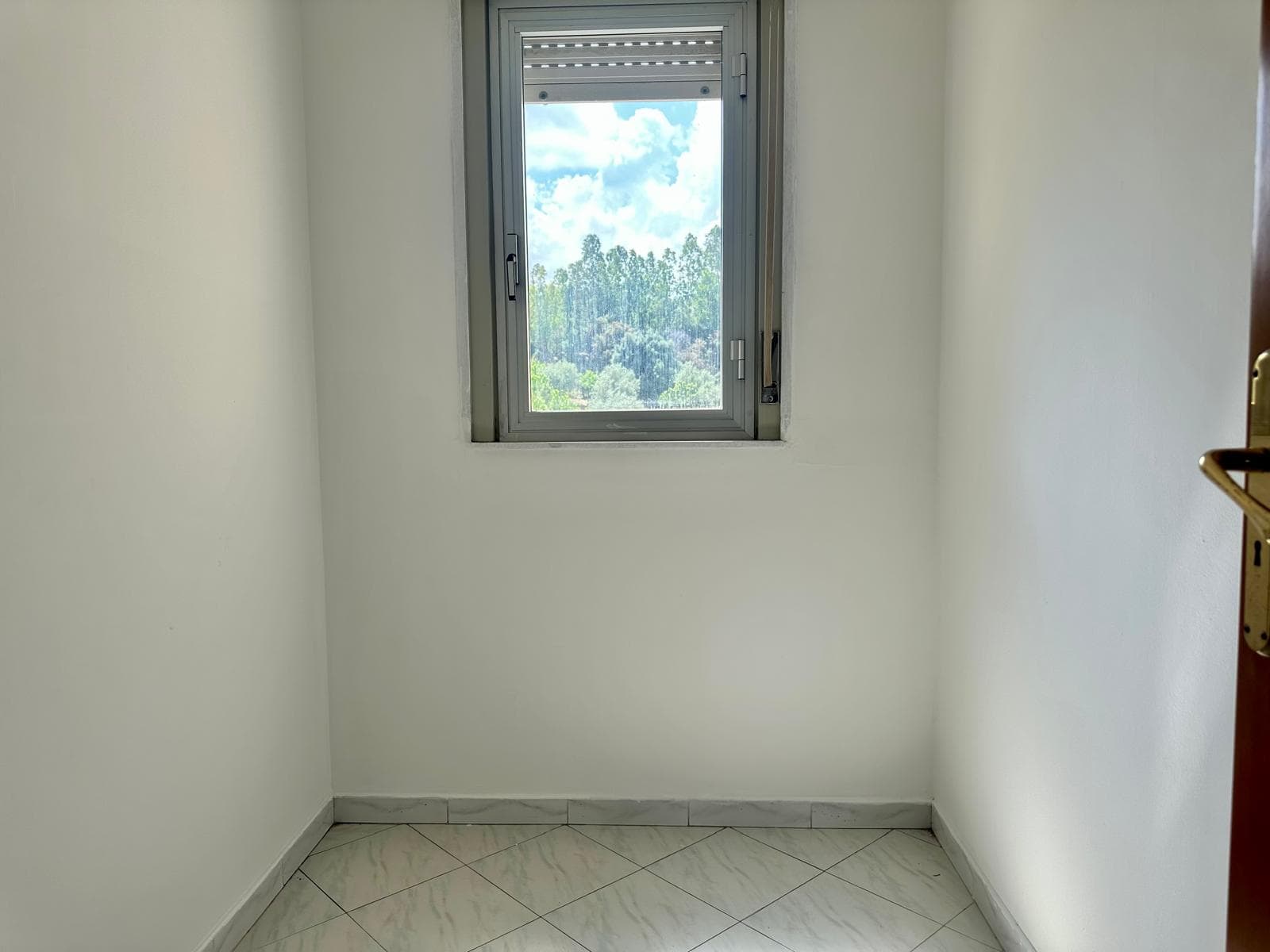 Finestra in una stanza luminosa con vista su un paesaggio verde e cielo azzurro.