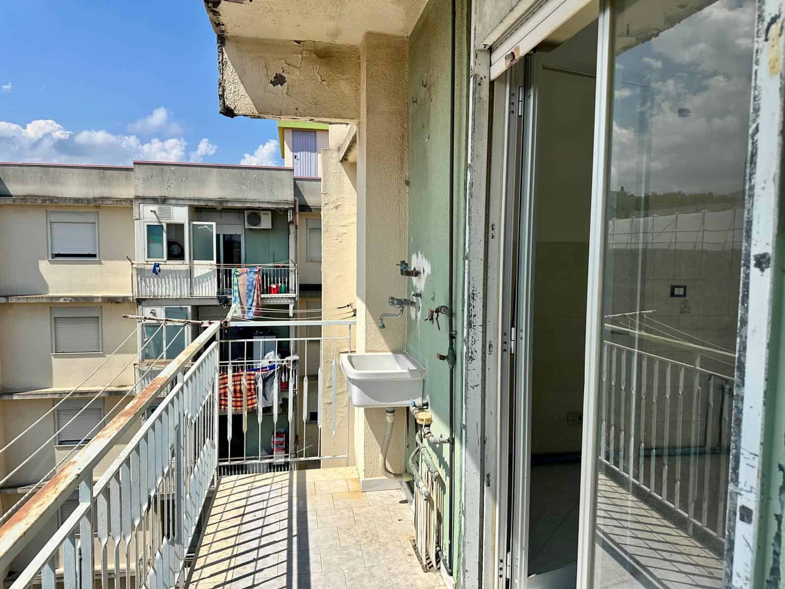 Balcone di un appartamento con lavandino esterno e vista su altri edifici residenziali.
