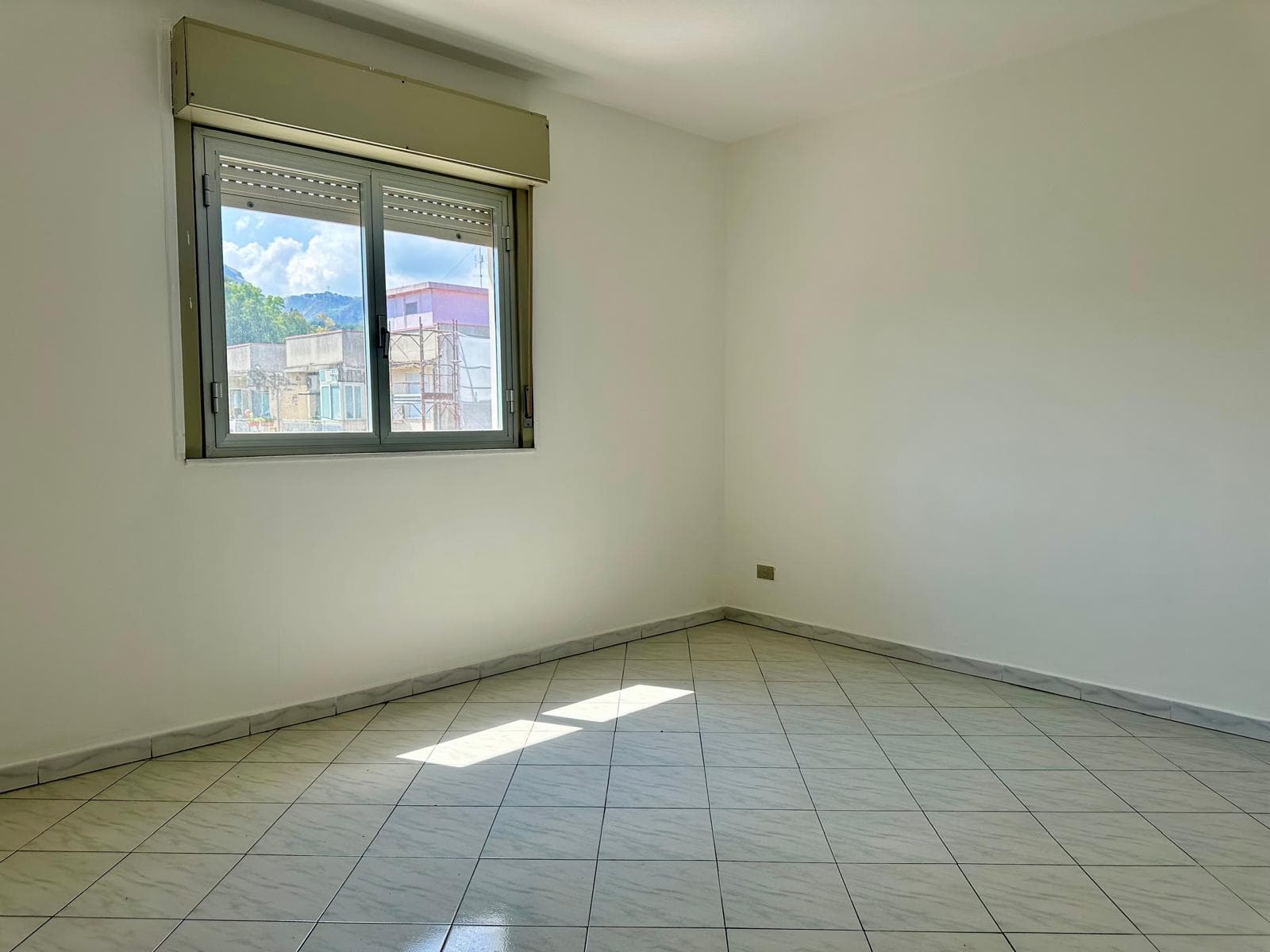 Stanza vuota in un appartamento in vendita con finestra e pavimento in piastrelle.