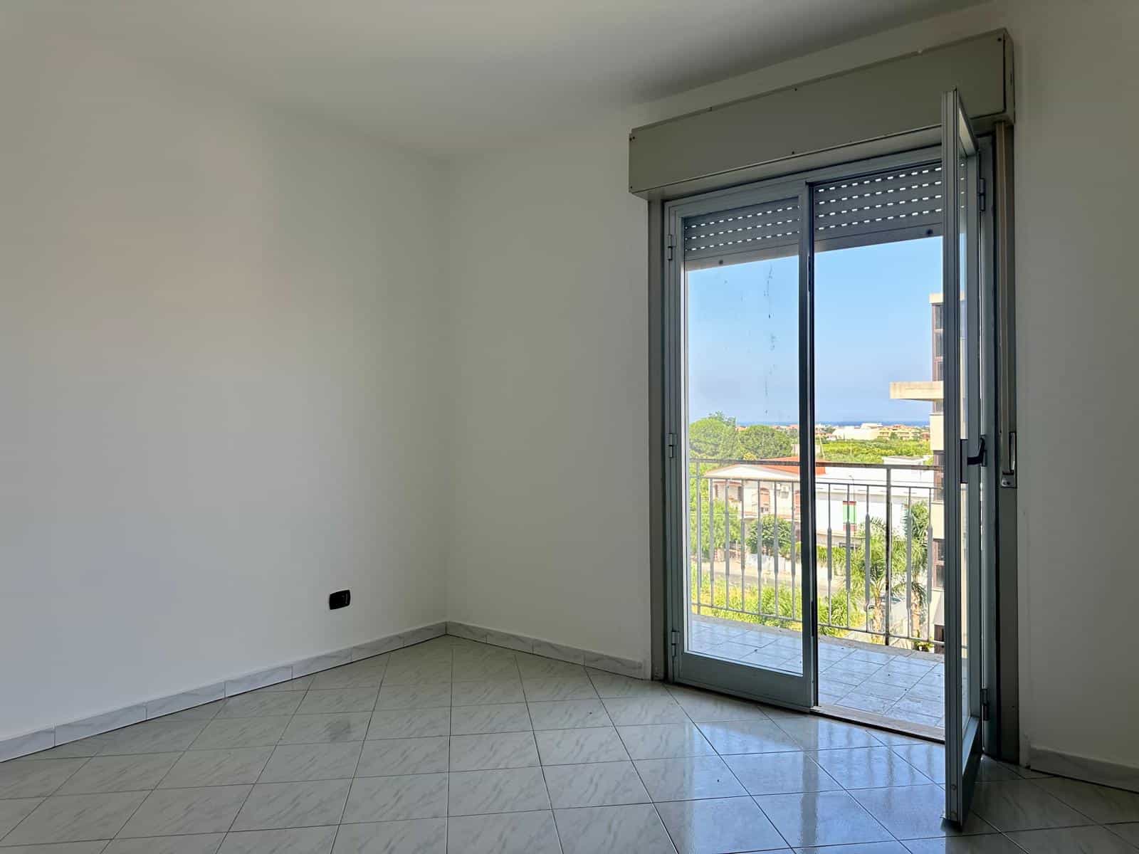 Stanza luminosa con porta finestra che dà su un balcone, vista panoramica sulla città e il verde.