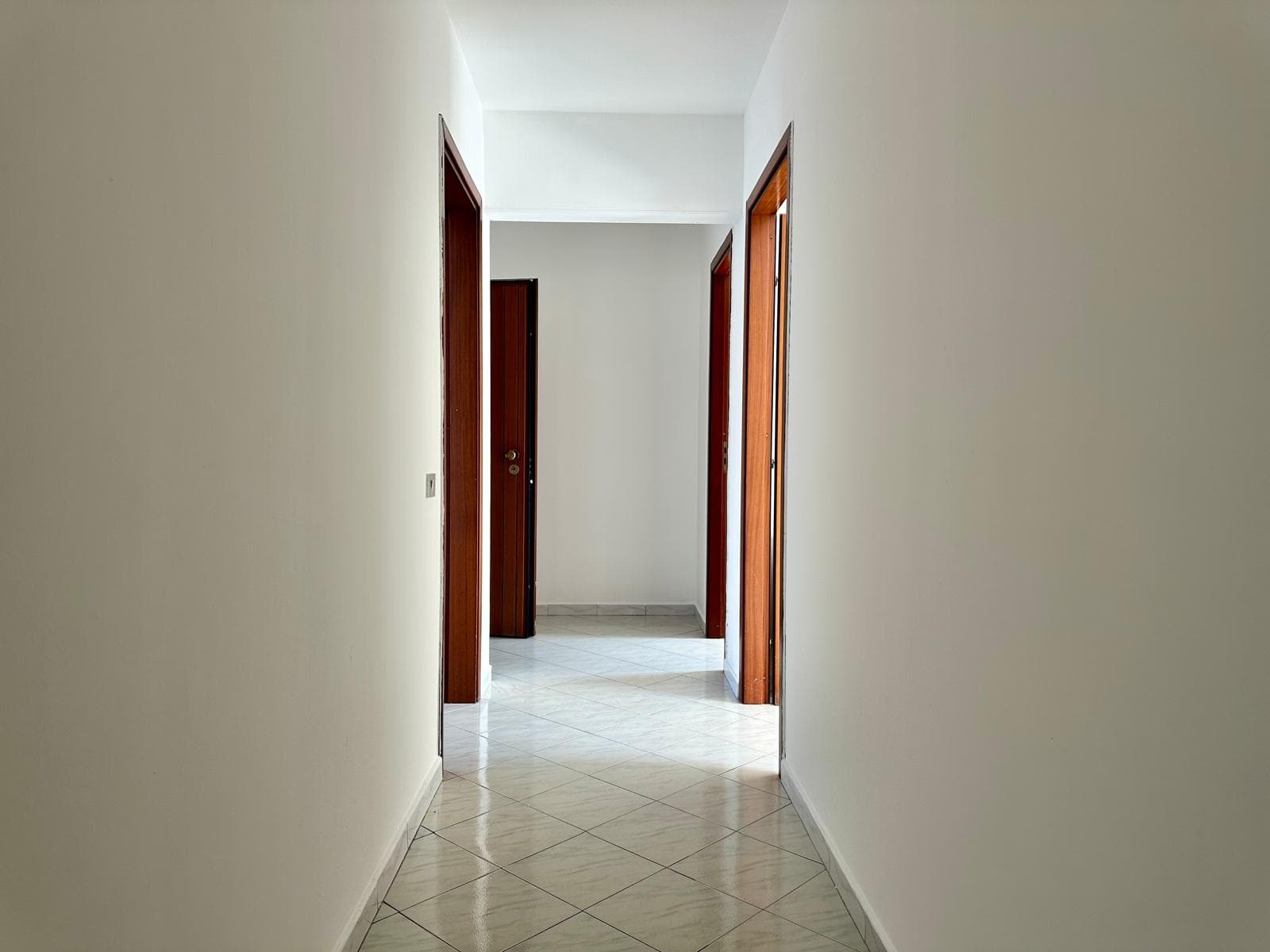 Corridor in un appartamento in vendita con pareti bianche e porte in legno scuro.