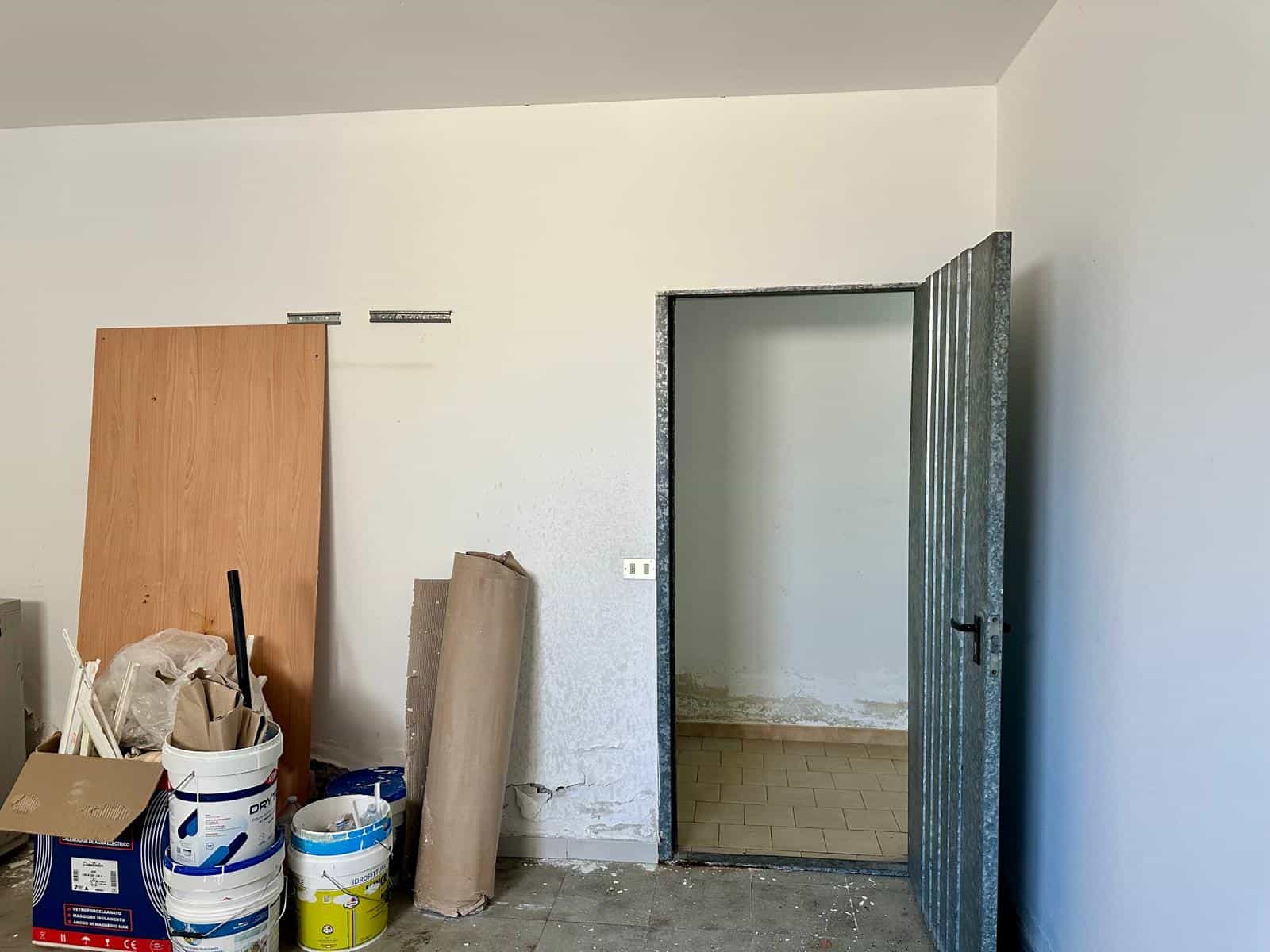 Interno di un appartamento in fase di ristrutturazione con pareti bianche e porta in metallo.