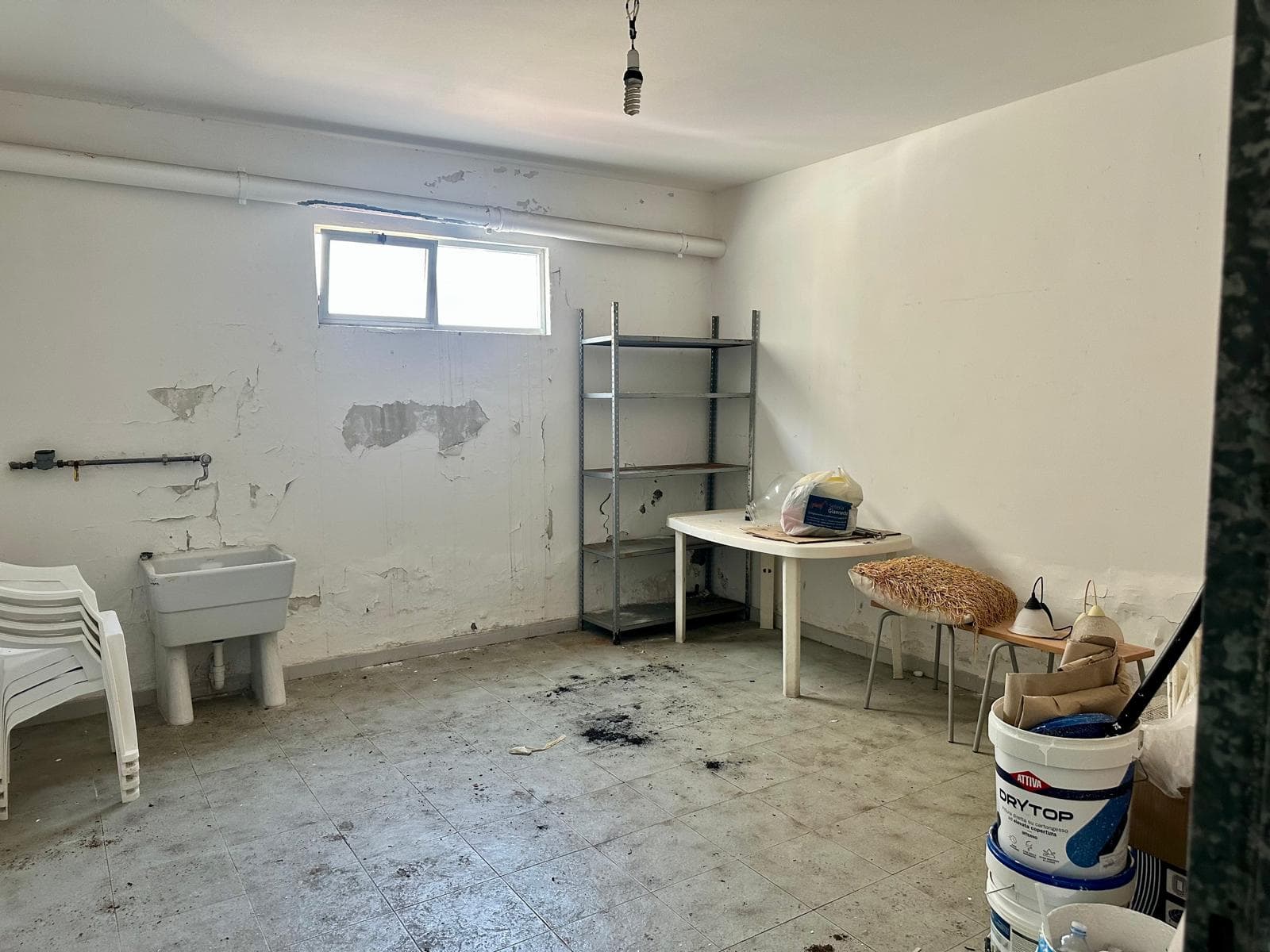 Interno di un appartamento in vendita con pareti danneggiate e pavimento usurato, spazio vuoto con pochi mobili e finestra piccola.