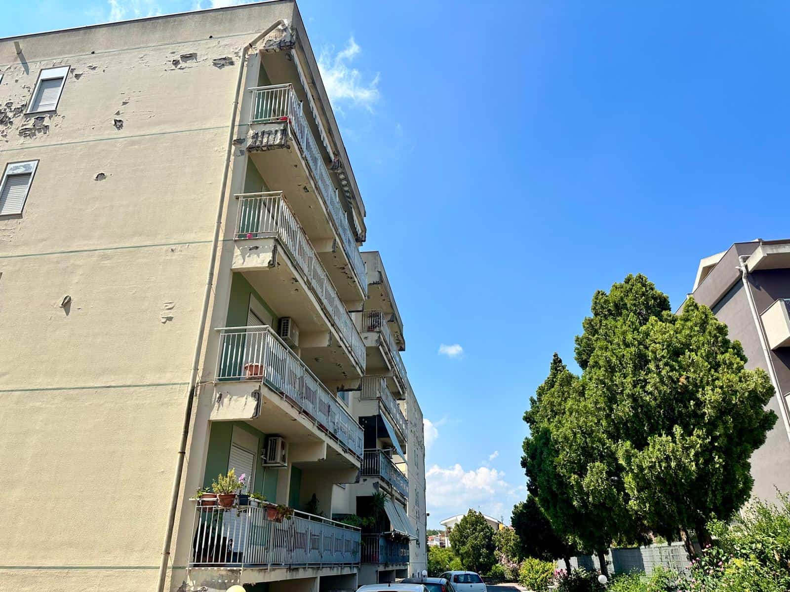 Appartamento in vendita in via Delle Ginestre, vista esterna di un edificio residenziale con balconi e piante, sotto un cielo sereno.
