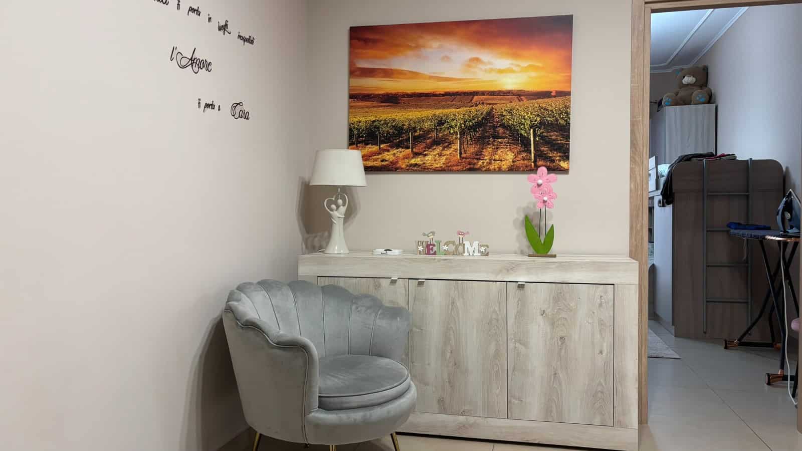 Interno di un appartamento in vendita a Milazzo, vista su una credenza bianca con decorazioni e una sedia grigia in stile vintage.