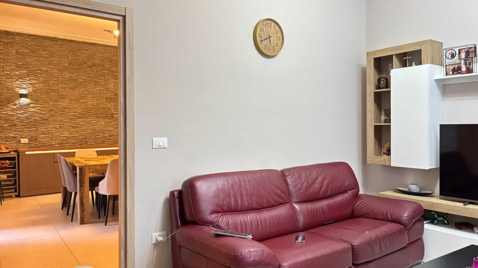 Salotto accogliente con divano rosso e pareti chiare, arredamento moderno e TV, in un appartamento in vendita a Milazzo.