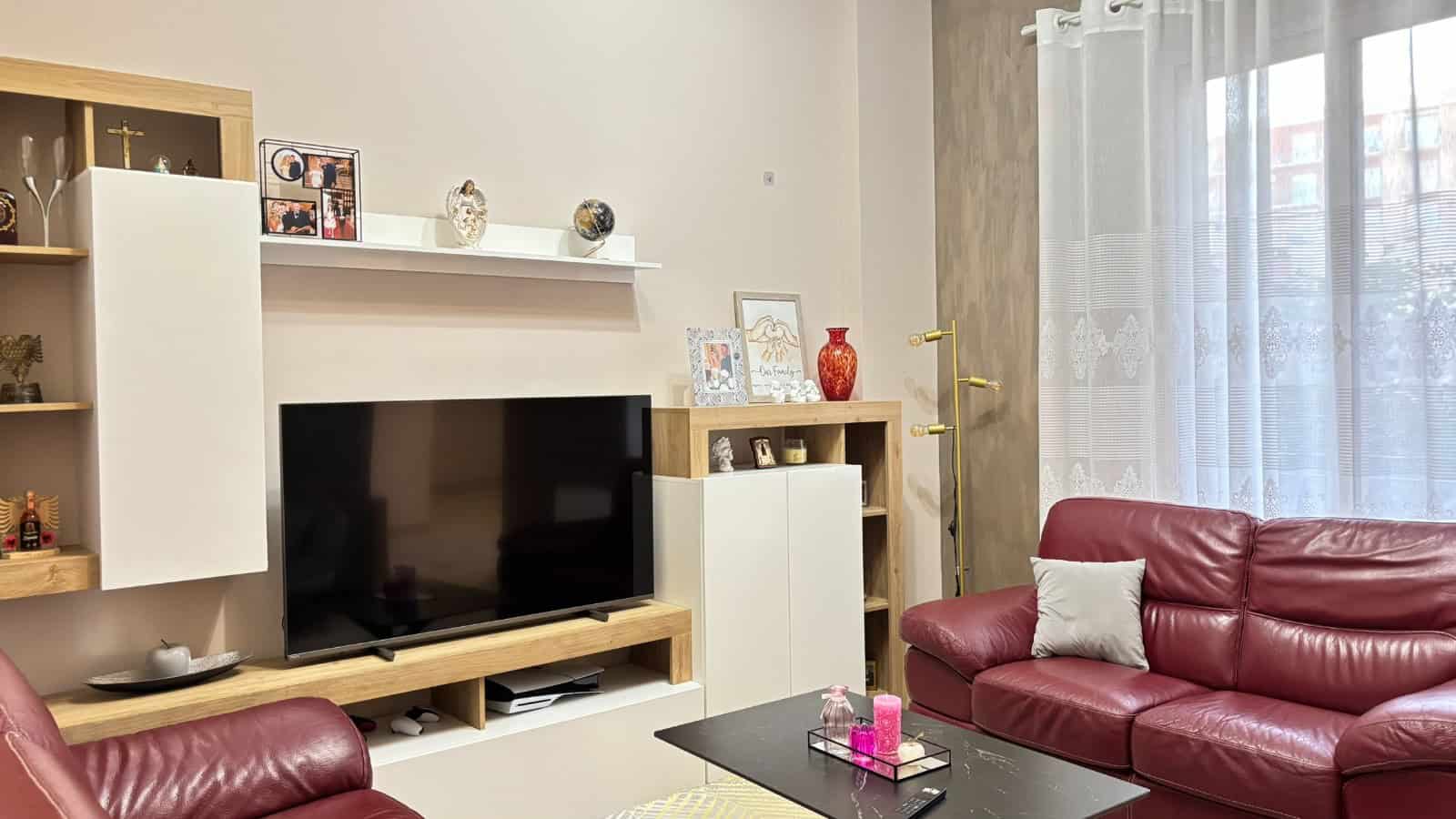 Salotto moderno con divani in pelle rossa, TV e decorazioni eleganti, in un appartamento in vendita a Milazzo.