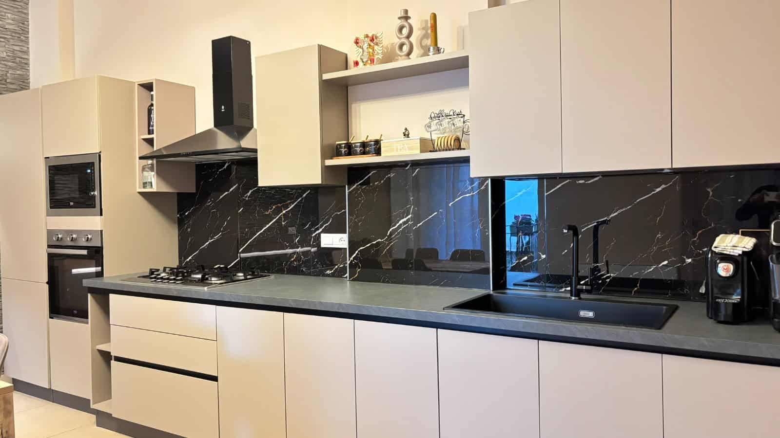 Cucina moderna con mobili bianchi, piano in pietra nera e elettrodomestici integrati in un appartamento in vendita a Milazzo.