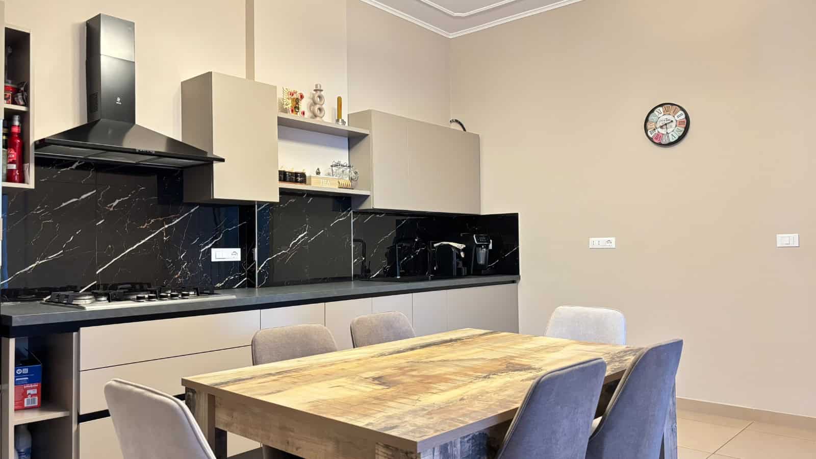 Interno moderno di un appartamento con cucina a vista e zona pranzo con tavolo in legno e sedie imbottite.