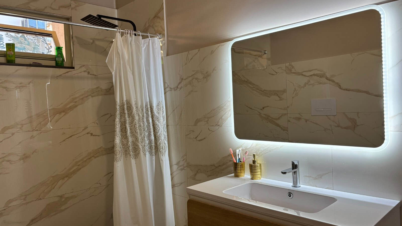 Bagno moderno con pareti in marmo e specchio con illuminazione a LED, dettagli eleganti e funzionali.